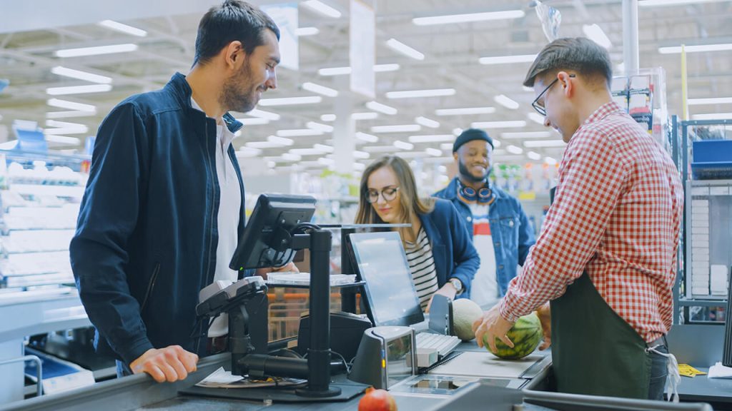 man-checkered-shirt-stands-cashier-while-customer-checks-his-produce